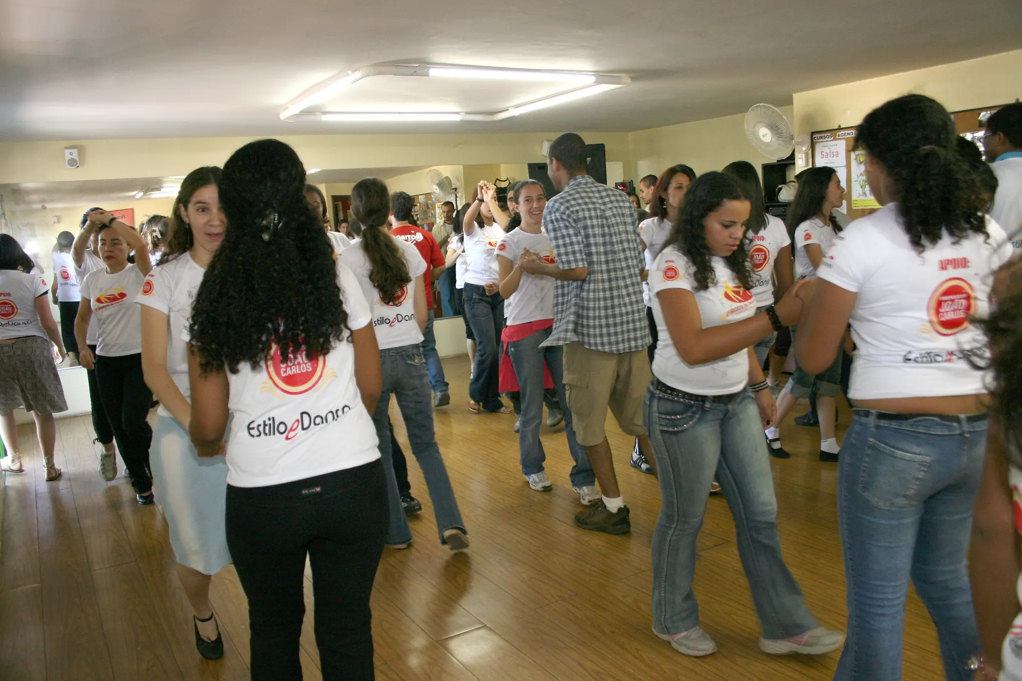 Duplas praticam dança em salão ocupado por participantes