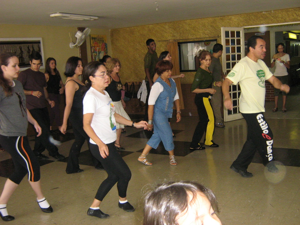 Grupo de participantes acompanha atividade coletiva de dança conduzida no salão