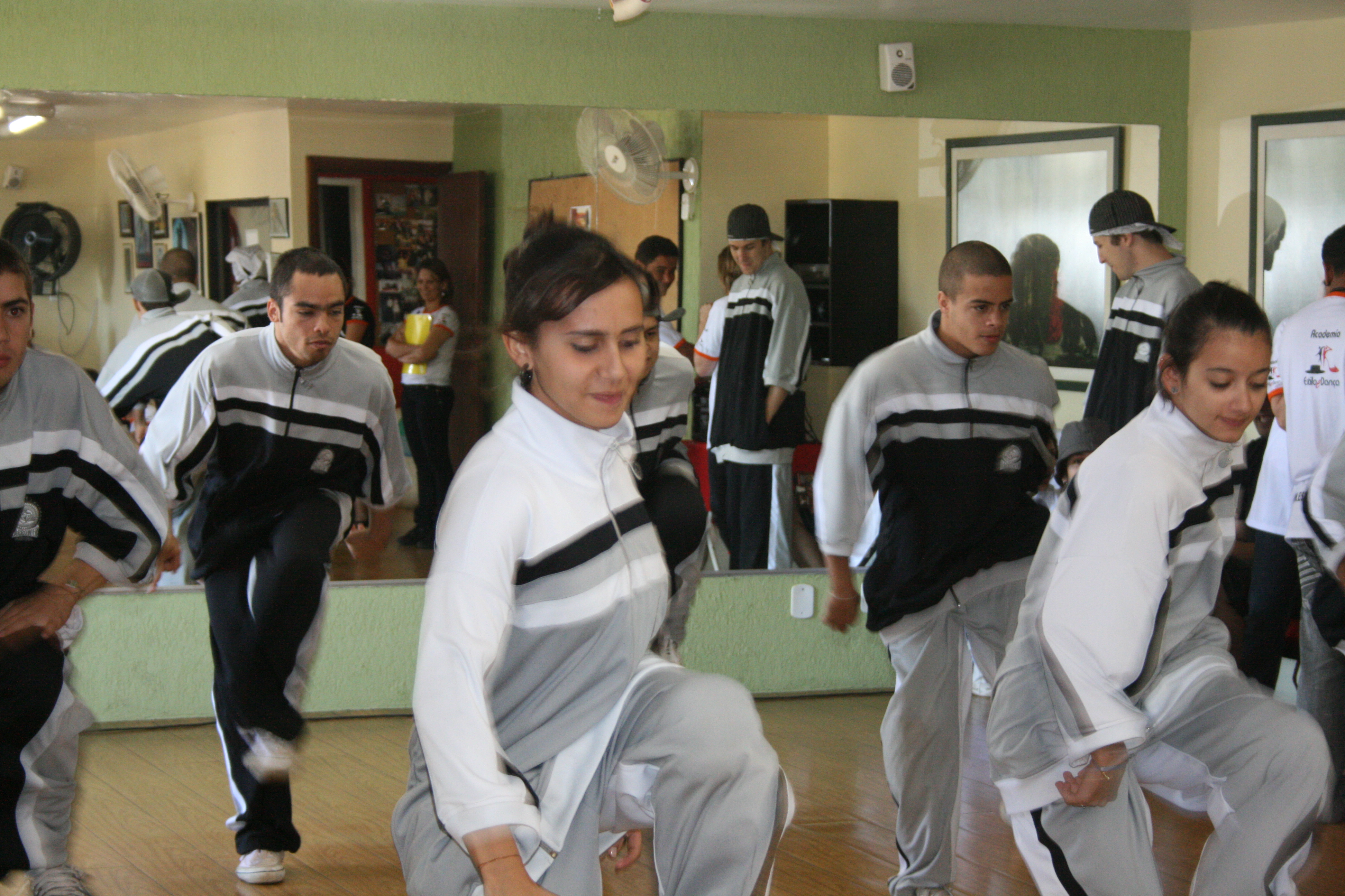 Três participantes com trajes brancos e pretos executam coreografia