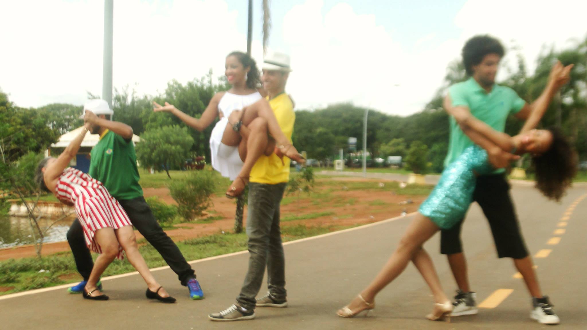 Três duplas realizam movimentos de dança em uma via de parque, com figurinos em diferentes cores.
