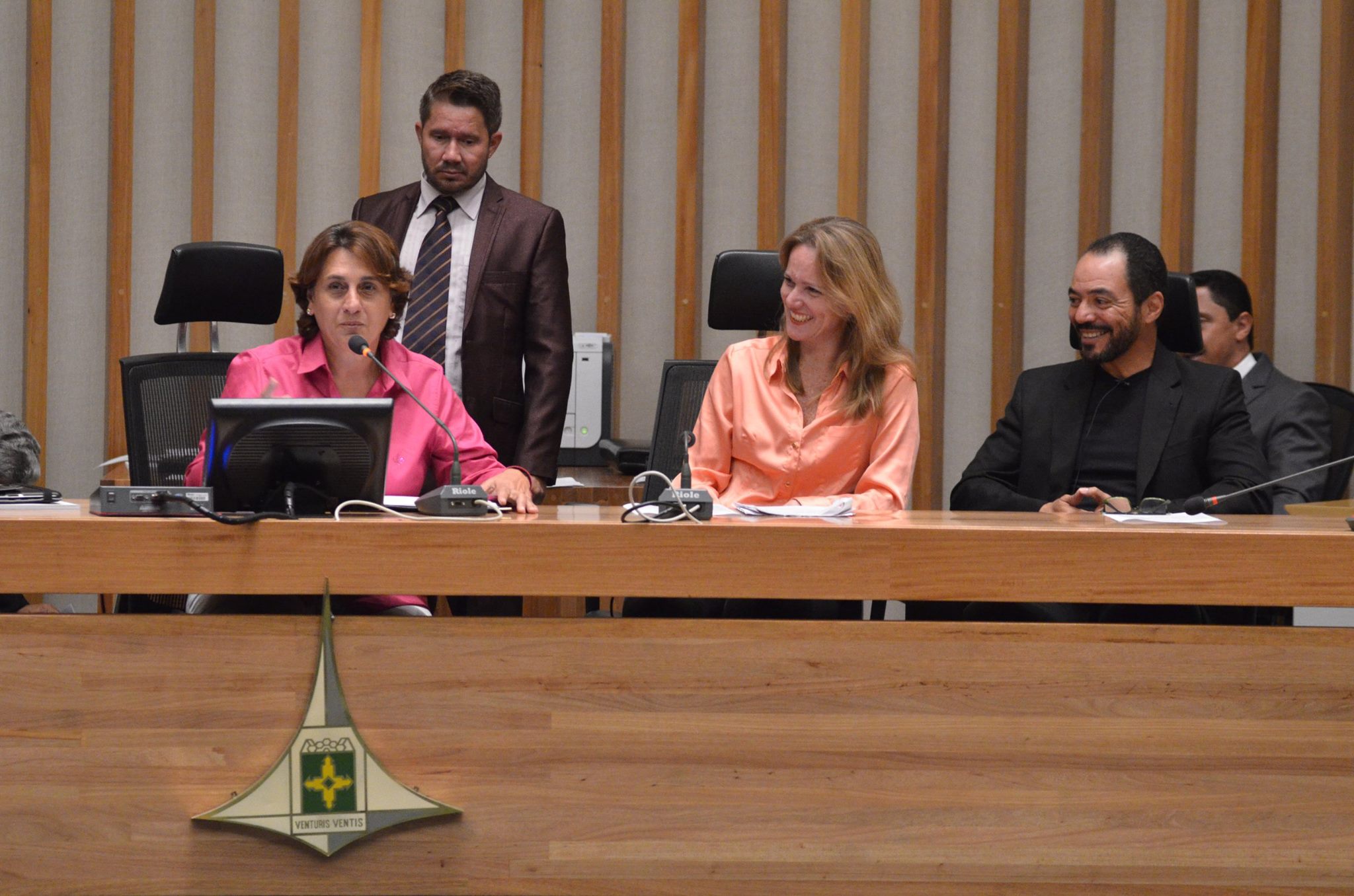 Três participantes ocupam a mesa principal de um plenário durante atividade institucional.