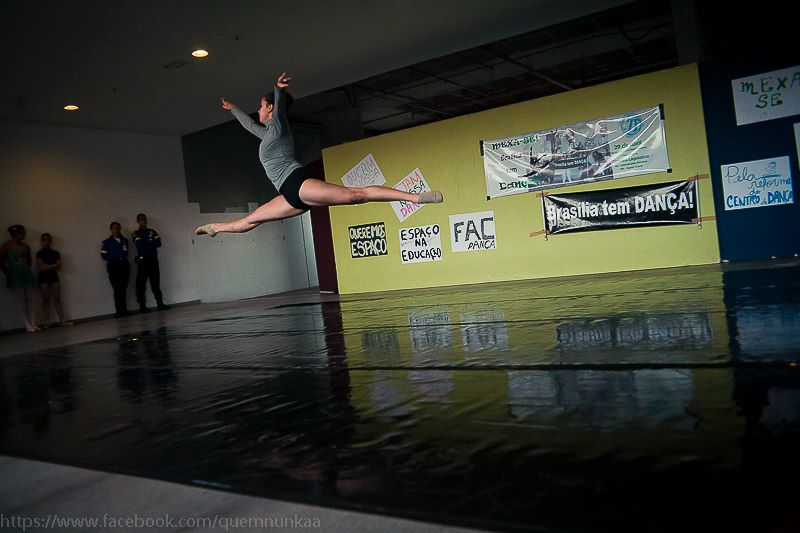 Dançarina executa um salto sobre o piso de apresentação diante de faixas e mensagens do movimento MEXA-SE!.