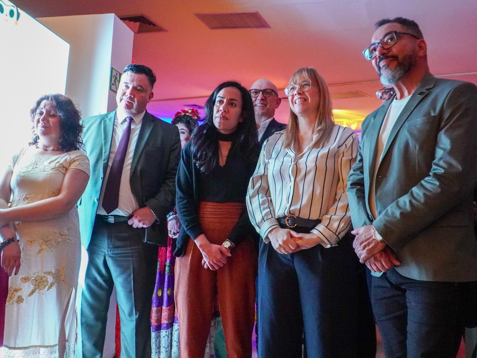 Participantes acompanham atividade de Día de Muertos em espaço interno com iluminação avermelhada
