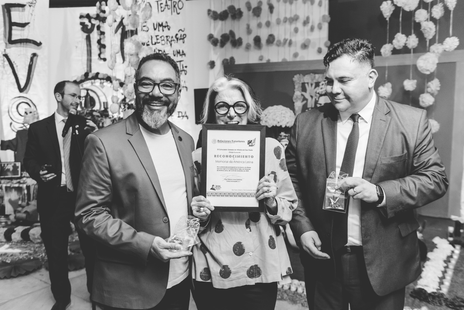 João Carlos Corrêa e dois participantes seguram certificado e lembranças durante entrega de reconhecimento pelo apoio do Memorial às atividades culturais do México