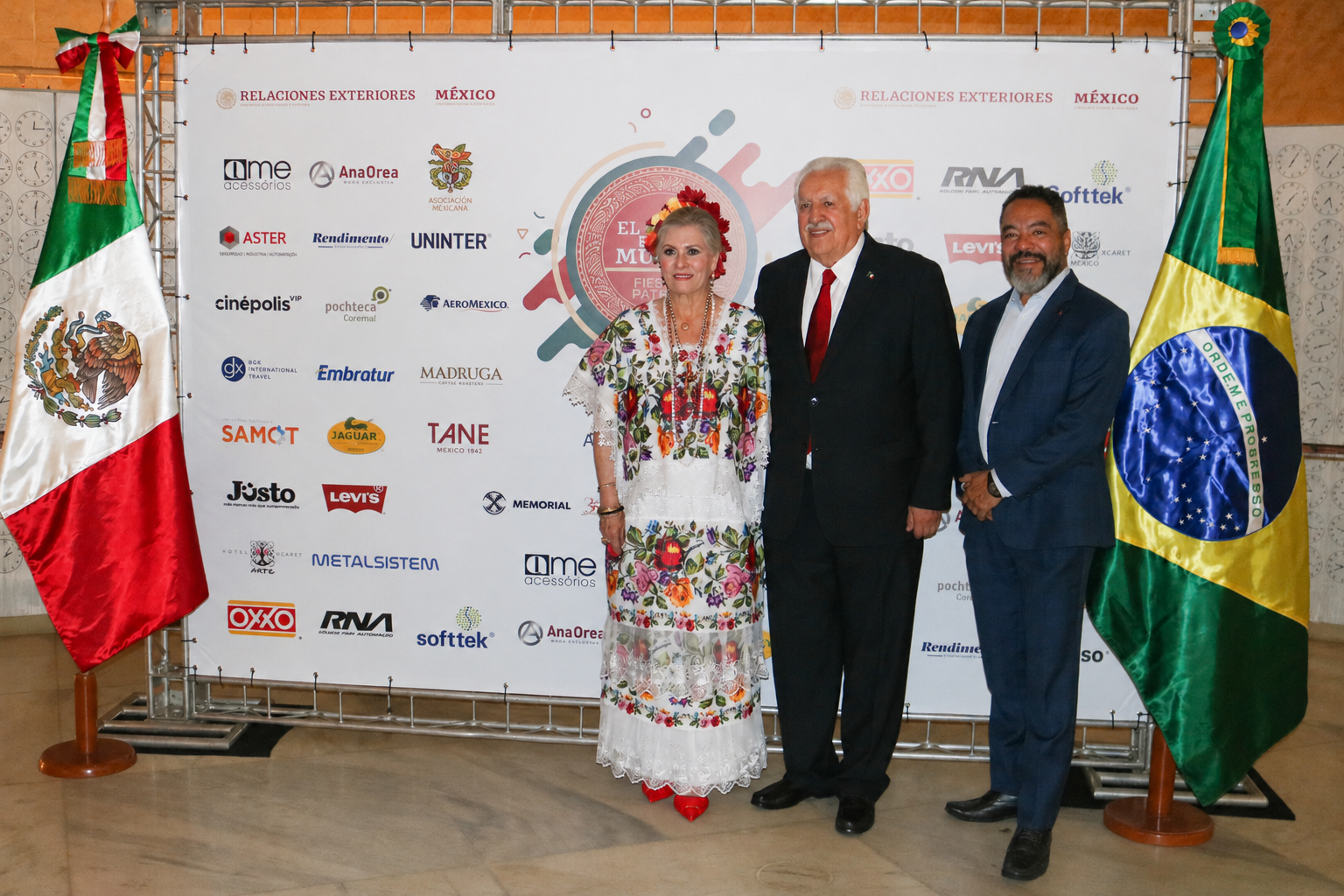 Raúl Bolaños-Cacho Guzmán com dois participantes diante de painel institucional e bandeiras do México e do Brasil