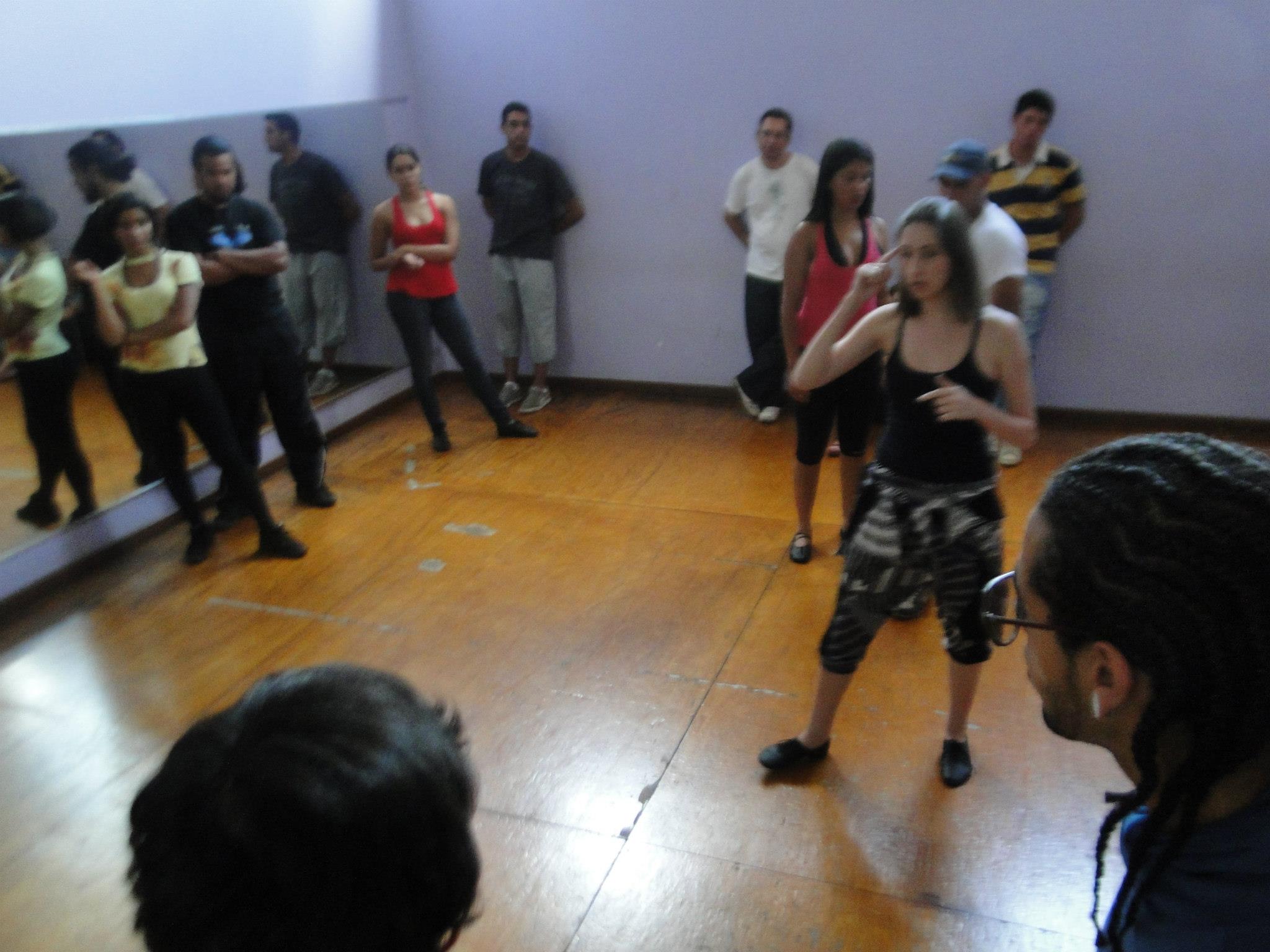 Mulher gesticula no centro de um estúdio enquanto um grupo de participantes acompanha a explicação.