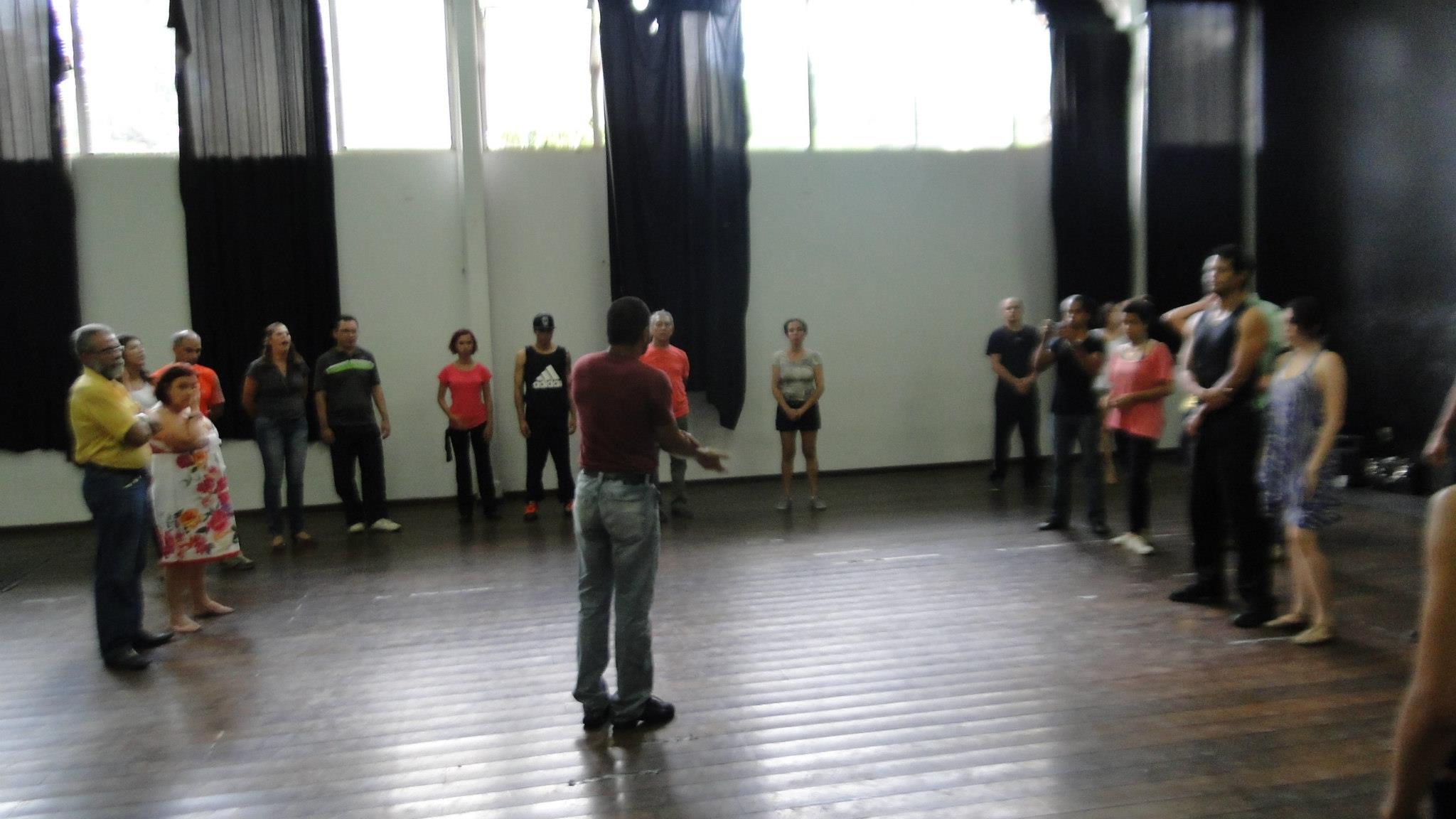 Participantes formam um semicírculo em torno de um homem que orienta o grupo no salão de dança.