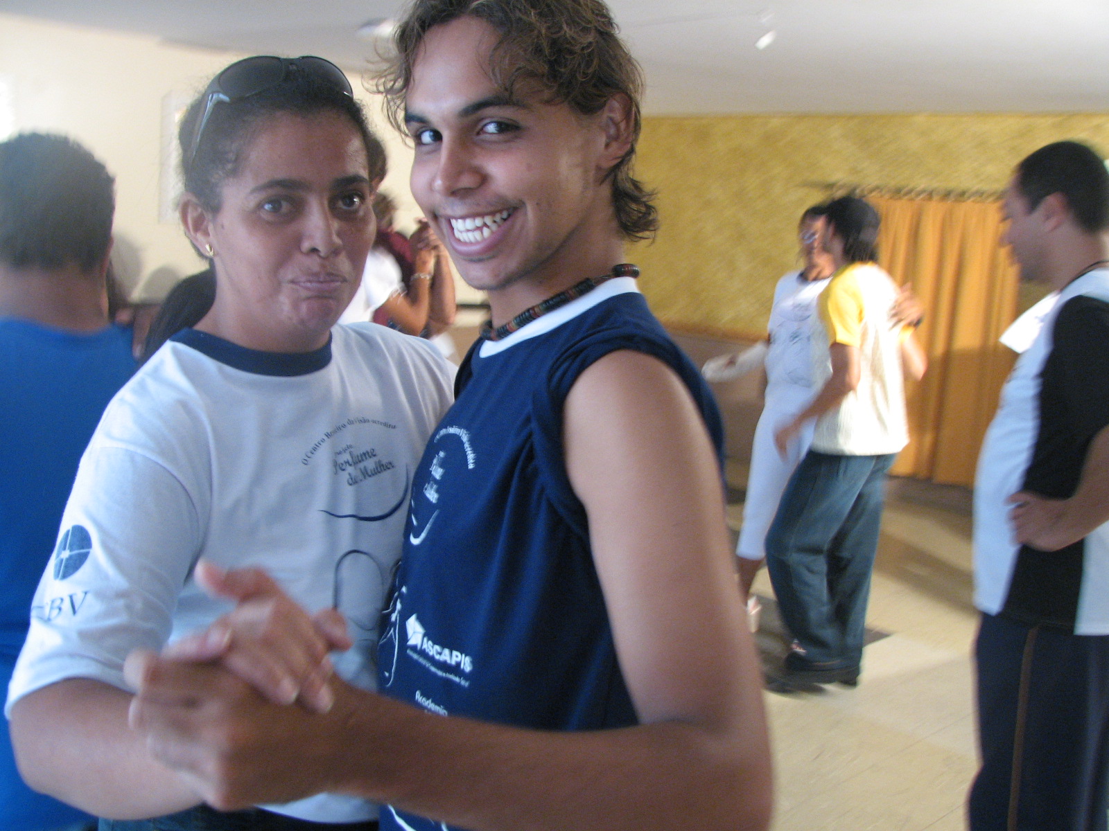 Dupla pratica condução em posição de dança com outros participantes ao fundo