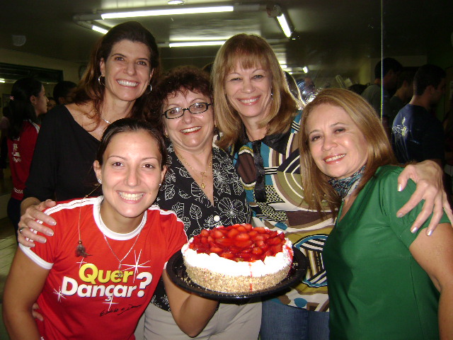 Participante com camiseta vermelha segura um bolo ao lado de outras quatro participantes