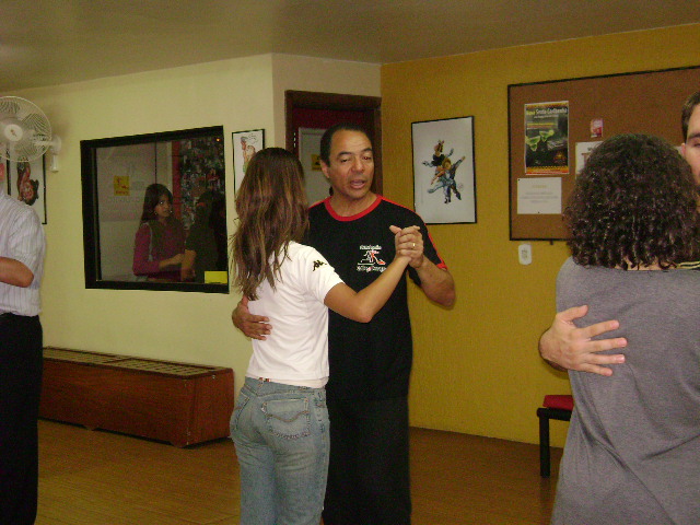 Duas duplas praticam dança de salão em diferentes áreas do salão