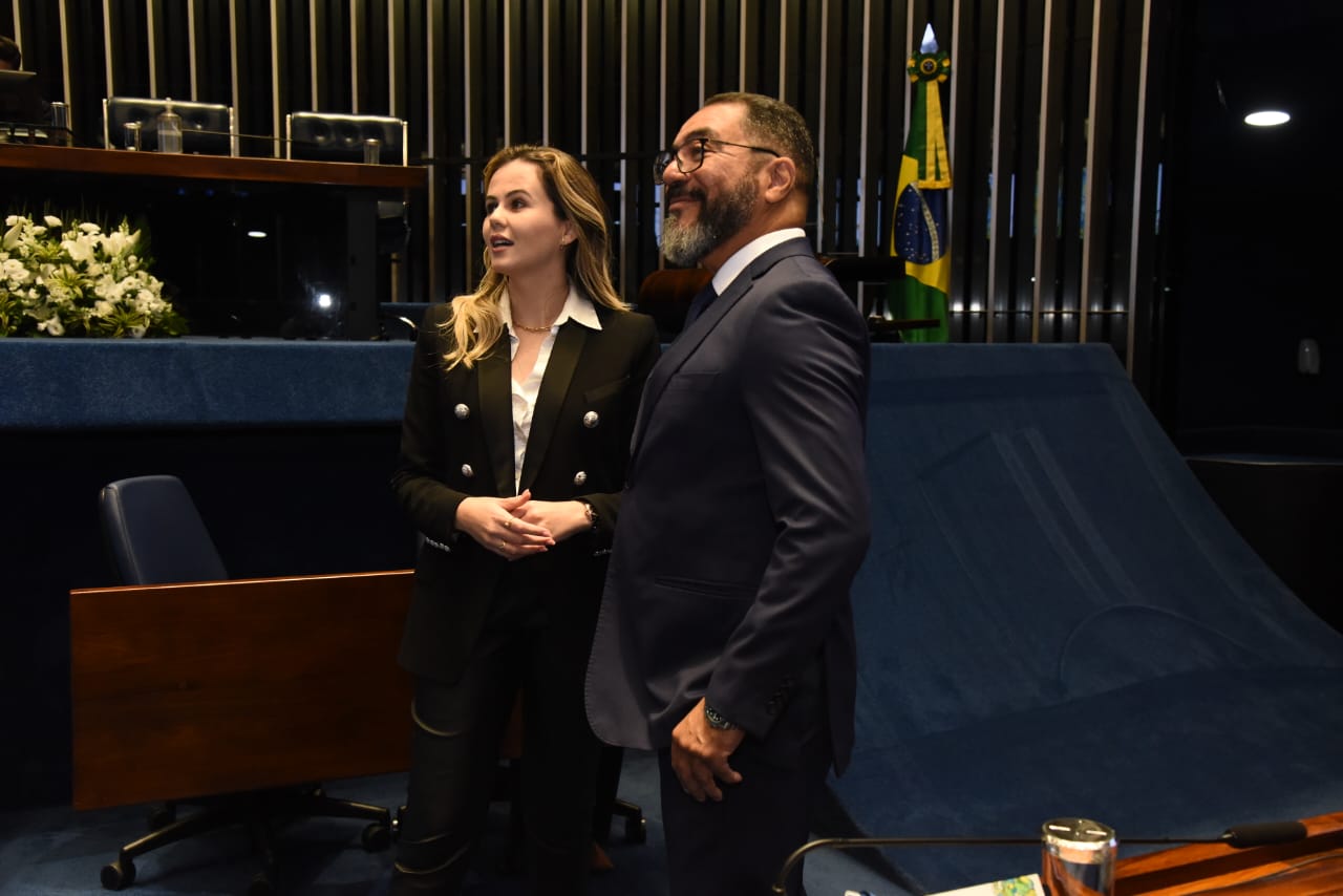 João Carlos Corrêa no plenário do Senado Federal, ao lado de uma representante parlamentar, com a bandeira do Brasil ao fundo