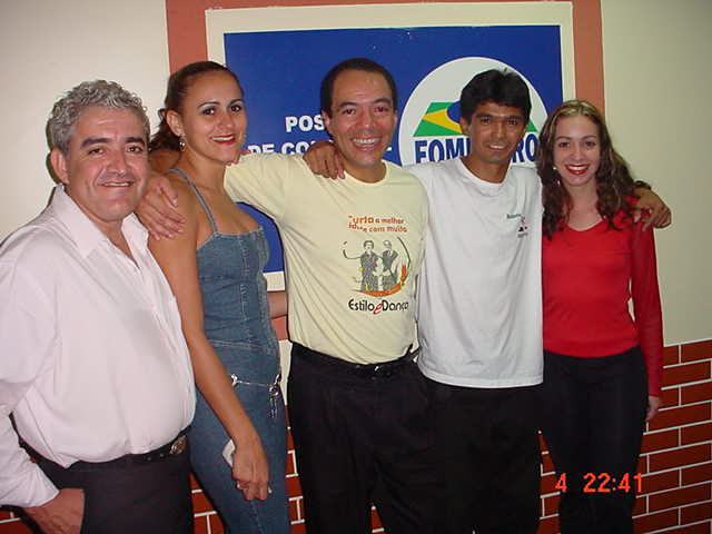 Cinco integrantes reunidos em retrato diante da identidade visual do evento