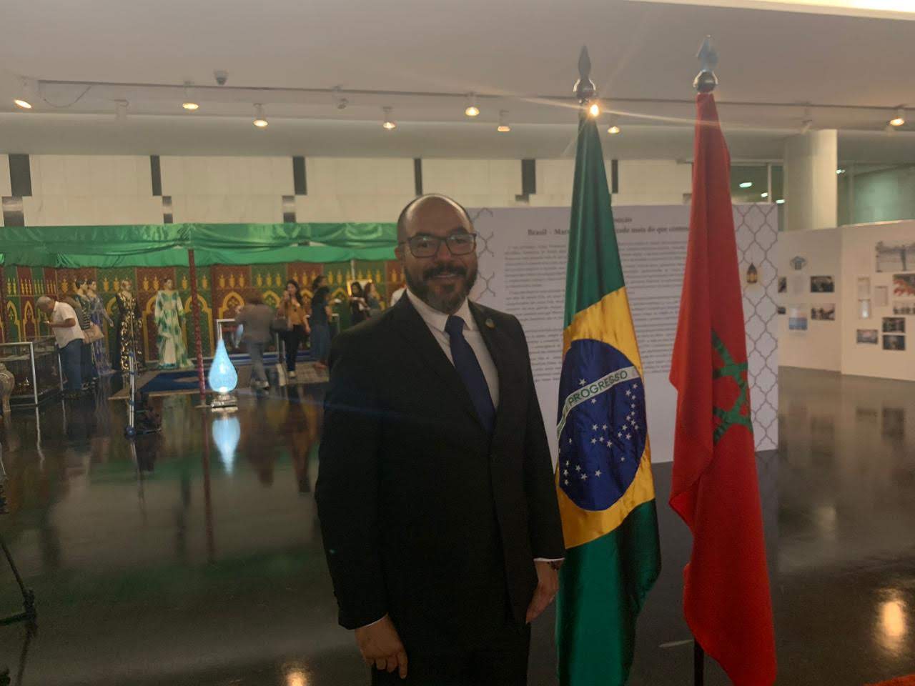 João Carlos Corrêa posa ao lado das bandeiras do Brasil e do Marrocos em salão expositivo.