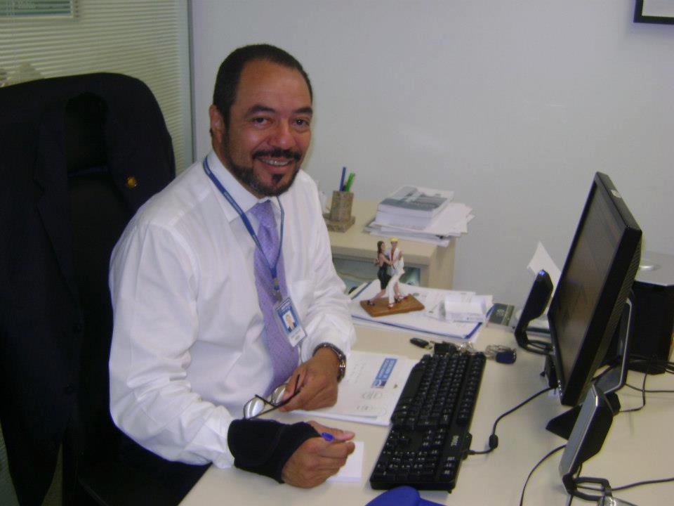 João Carlos Corrêa sentado à mesa de trabalho no gabinete, diante de computador, teclado e documentos.