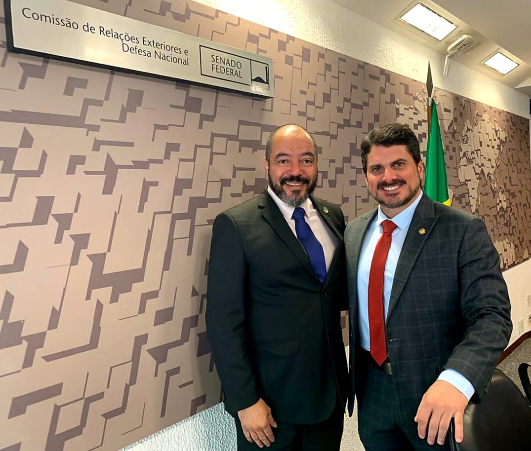 João Carlos Corrêa ao lado de um visitante diante da identificação da Comissão de Relações Exteriores e Defesa Nacional do Senado Federal.