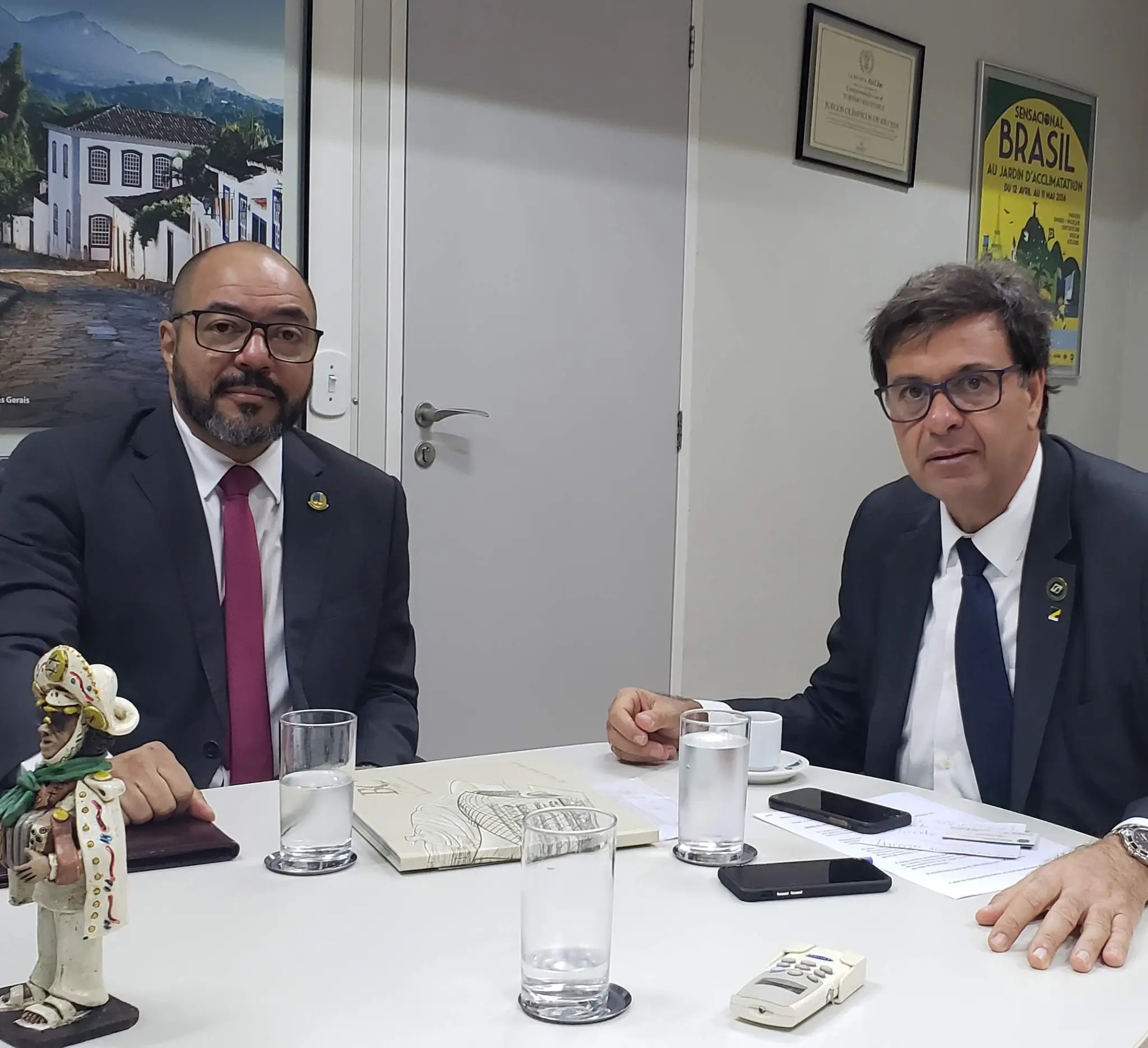 João Carlos Corrêa participa de audiência com o ministro do Turismo em mesa de gabinete com documentos e copos de água.