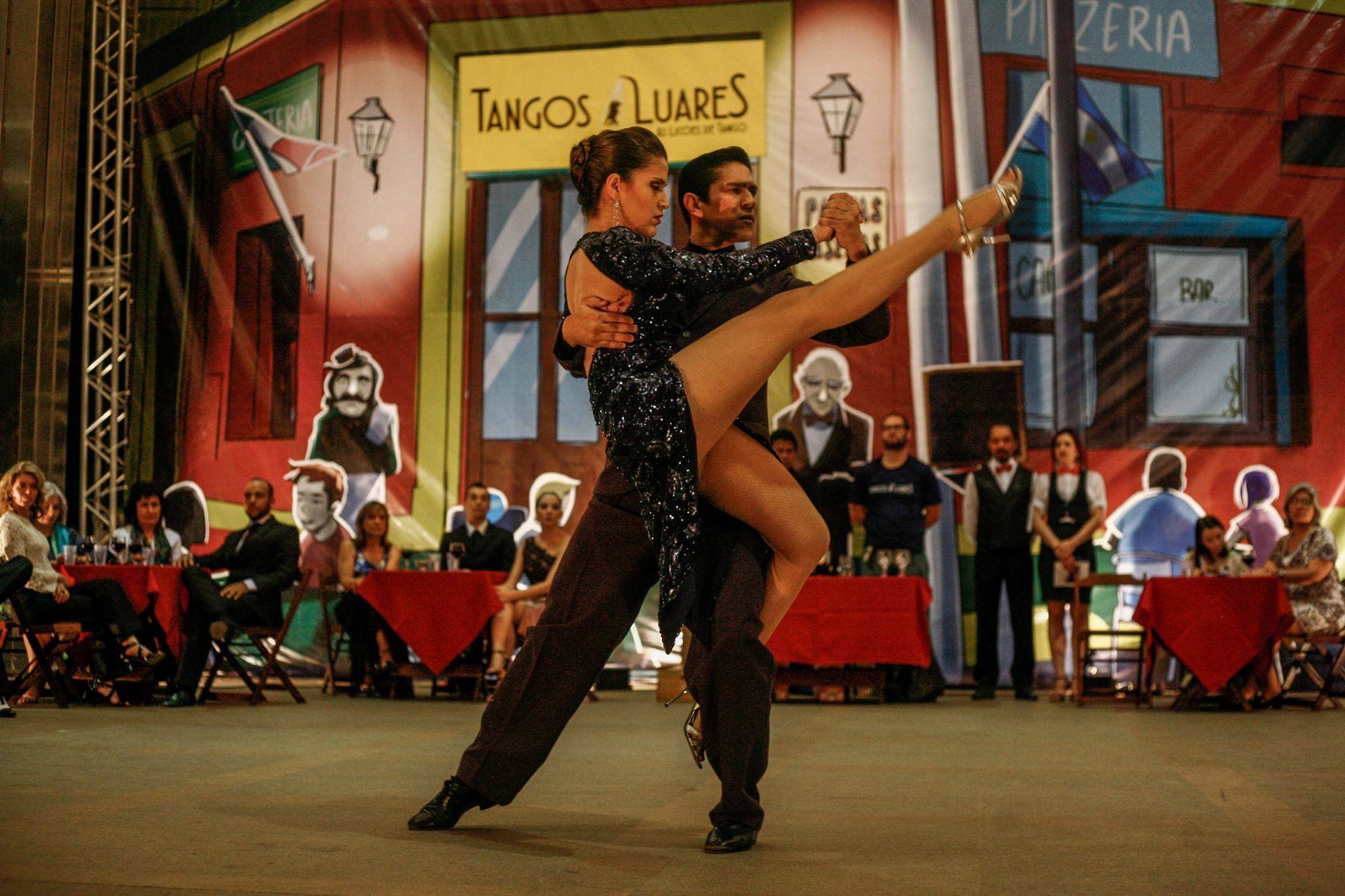 Casal dançando tango em apresentação do projeto Tangos e Luares, diante de cenário cenográfico inspirado em uma praça latino-americana