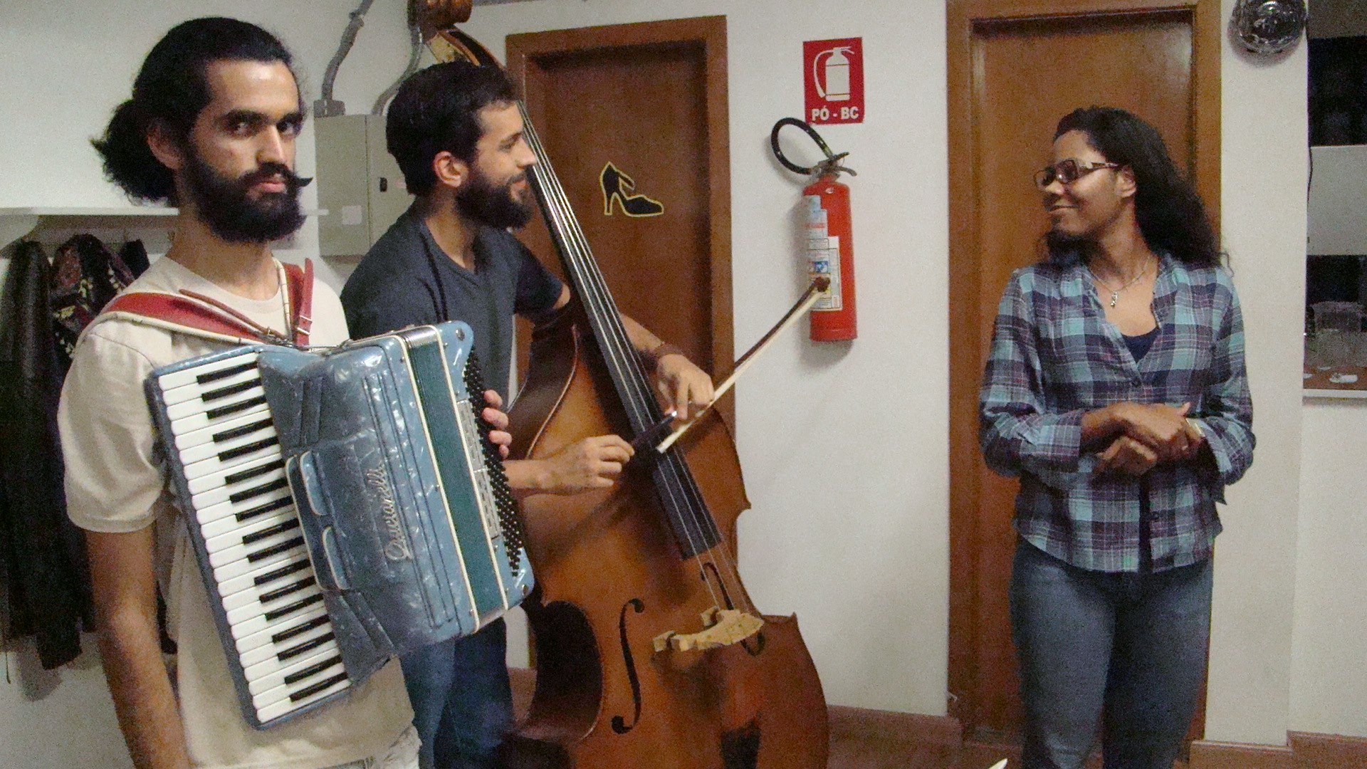 Músicos con acordeón y contrabajo conversan con un integrante del equipo durante la preparación de Tangos e Luares
