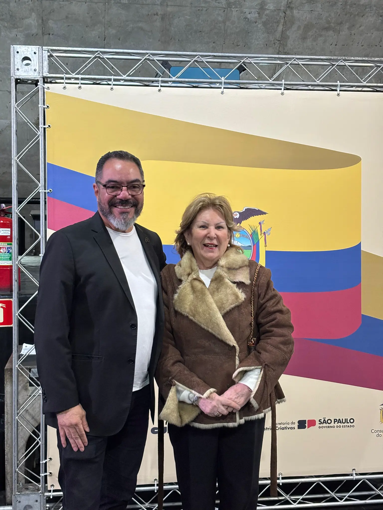 João Carlos Corrêa y Marta Echarte posan frente a un panel institucional durante un evento cultural diplomático en el Memorial