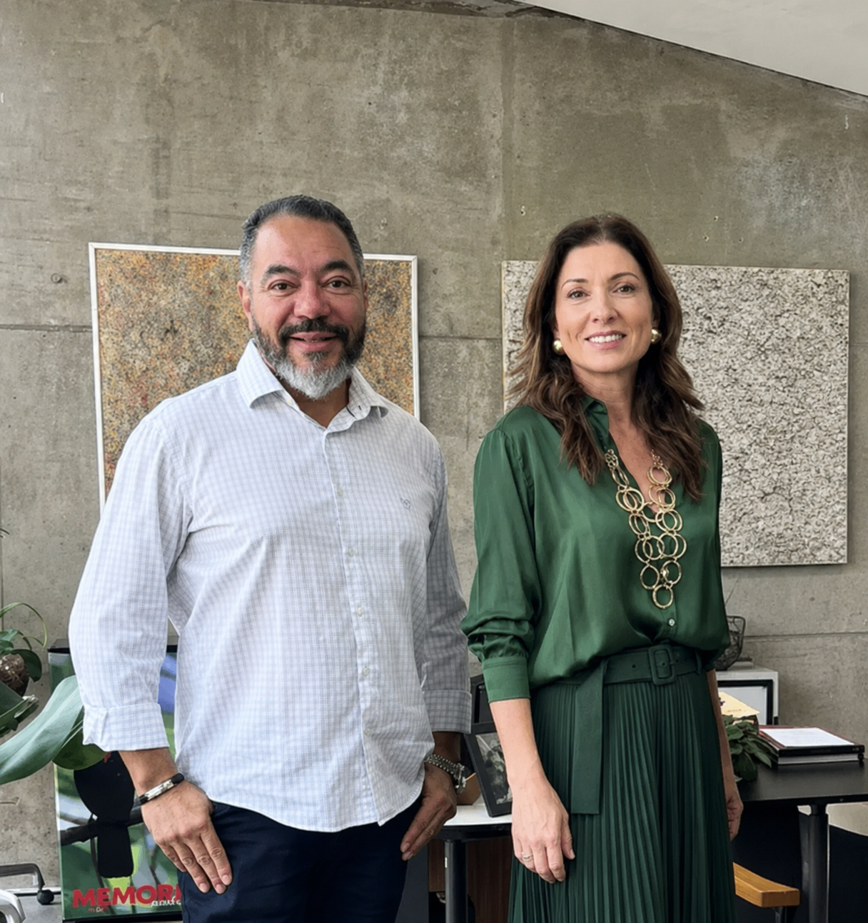 João Carlos Corrêa, con camisa clara, y Blanca Montilla, con vestido verde, posan uno junto a la otra frente a obras en una pared de concreto