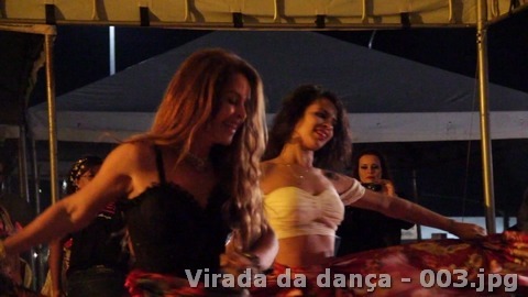 Duas mulheres movimentam saias coloridas em uma apresentação sob a estrutura coberta do evento.
