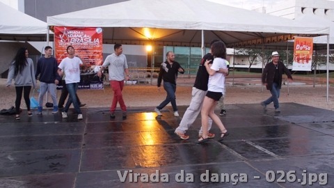 Grupo se apresenta em um palco sob estrutura coberta, com a identidade do evento ao fundo.