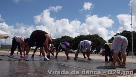Grupo realiza exercícios de alongamento sobre uma plataforma ao ar livre durante o dia.