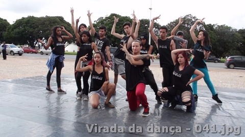 Grupo jovem realiza poses coreografadas sobre piso de dança em área externa.