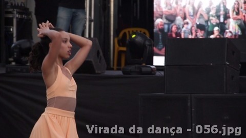 Jovem dançarina com traje em tom pêssego se apresenta no palco diante de equipamentos de som.
