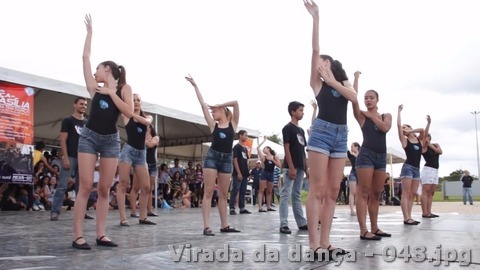 Grupo jovem realiza uma coreografia sincronizada em palco ao ar livre diante do público.
