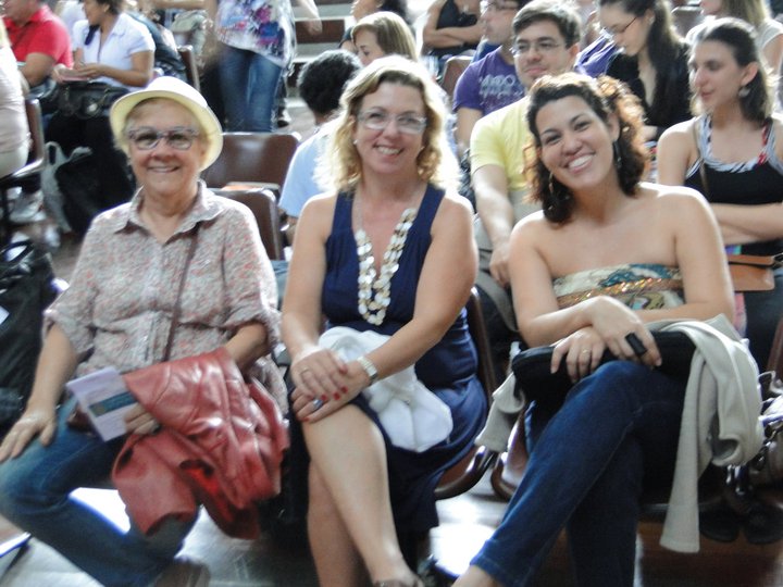 Três participantes sentadas na plateia acompanham a programação do XII Fórum Nacional de Dança.