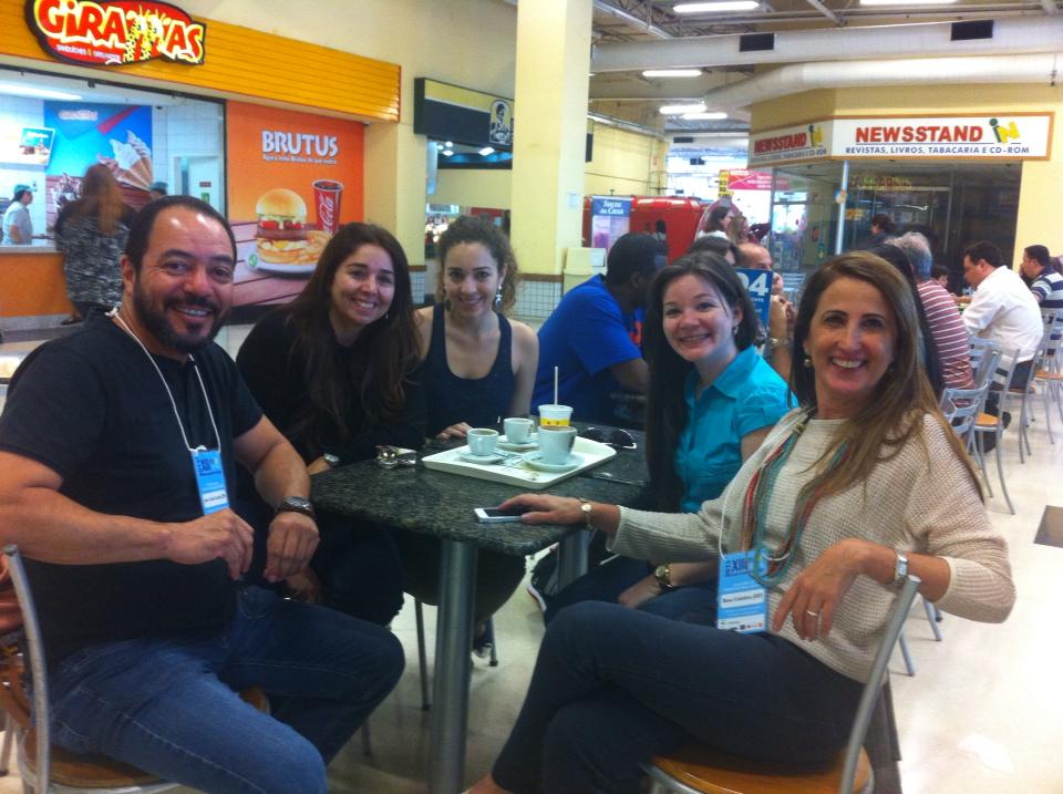 Cinco participantes credenciados conversam ao redor de uma mesa durante intervalo da programação.